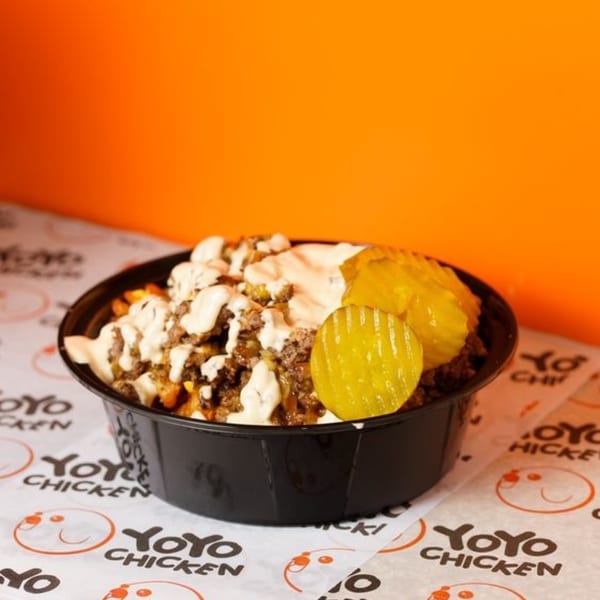 Yoyo Chicken's loaded fries with ground meat, sauce, and pickles in a black bowl.