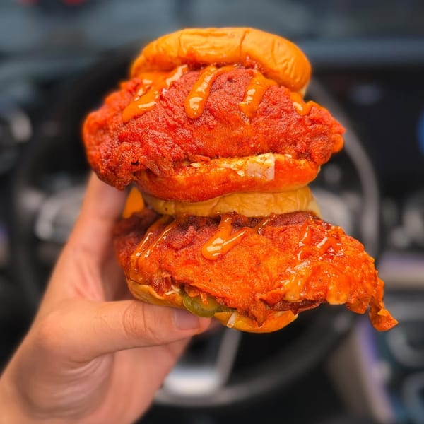 Hand holding a double-stacked Yoyo Chicken sandwich with spicy red fried chicken and sauce.