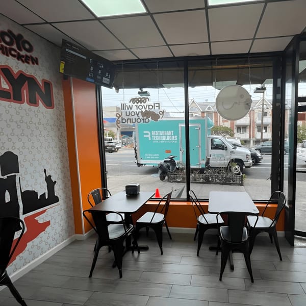 Interior of Yoyo Chicken with black tables and chairs, and a view of the street outside.