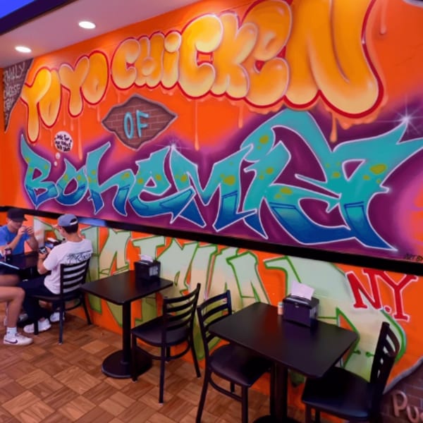 Two customers seated at tables in Yoyo Chicken, with vibrant graffiti art covering the walls.