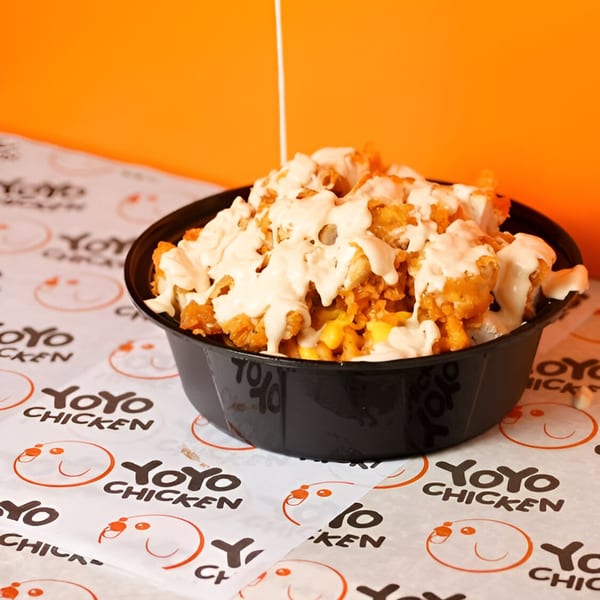 Yoyo Chicken's fried chicken and corn, drizzled with creamy sauce, in a black bowl.