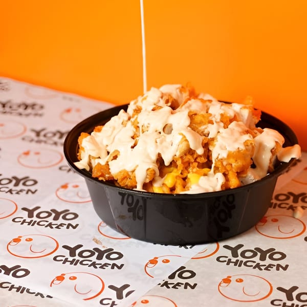 Yoyo Chicken's fried chicken bites and corn, drizzled with white sauce in a black bowl.