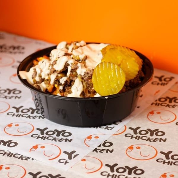 Yoyo Chicken bowl with fried chicken, sauce, and pickles on branded paper.