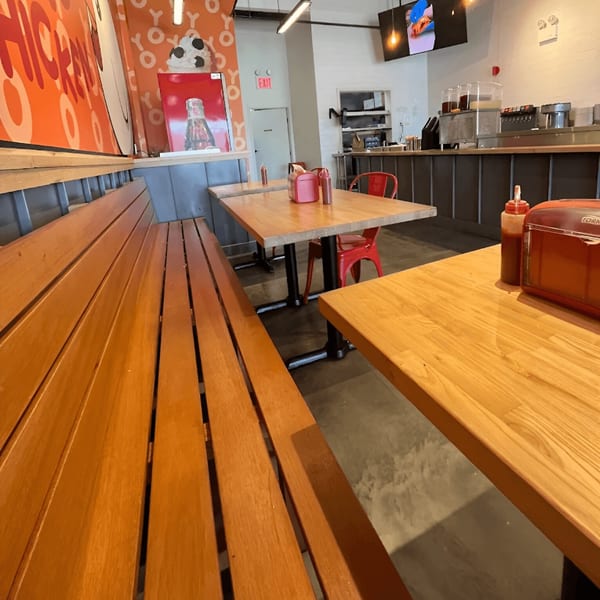 Interior of Yoyo Chicken with wooden benches, tables, red chairs, and a counter with drink dispensers.