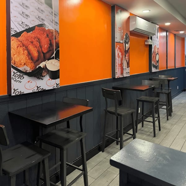 Interior of Yoyo Chicken with orange walls, dark tables, and fried chicken posters.