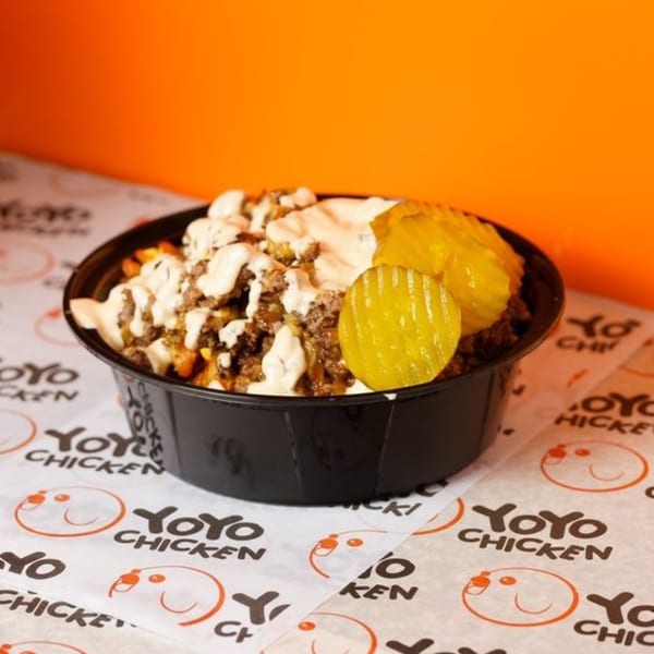 Yoyo Chicken's loaded fries with ground meat, white sauce, and pickles in a black bowl.