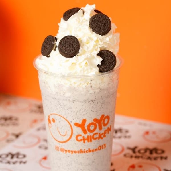 Yoyo Chicken's Oreo milkshake, topped with whipped cream and whole Oreo cookies, against an orange background.