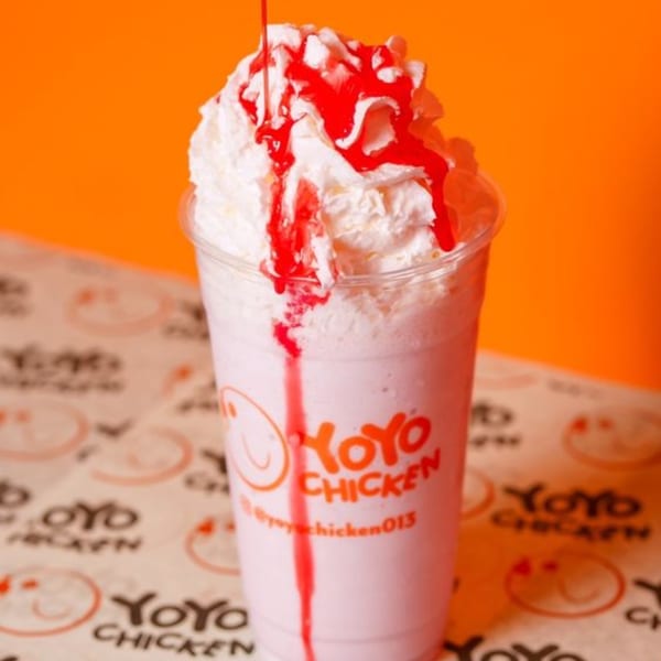 Yoyo Chicken strawberry milkshake with whipped cream and red syrup drizzle on a branded paper.