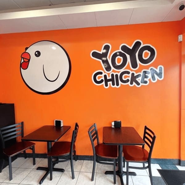 Interior of Yoyo Chicken with orange walls, a chicken logo, and two dark tables with chairs.