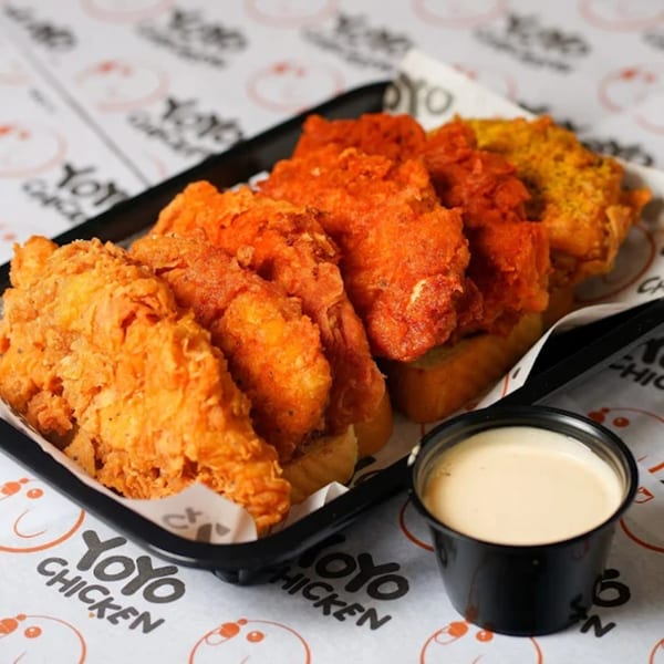 A black tray of Yoyo Chicken's fried chicken tenders in various flavors, with a side of dipping sauce.