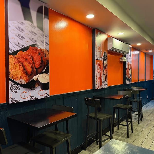 Interior of Yoyo Chicken with orange and blue walls, high tables, and fried chicken posters.