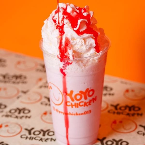 Yoyo Chicken strawberry milkshake with whipped cream and red syrup drizzle against an orange background.