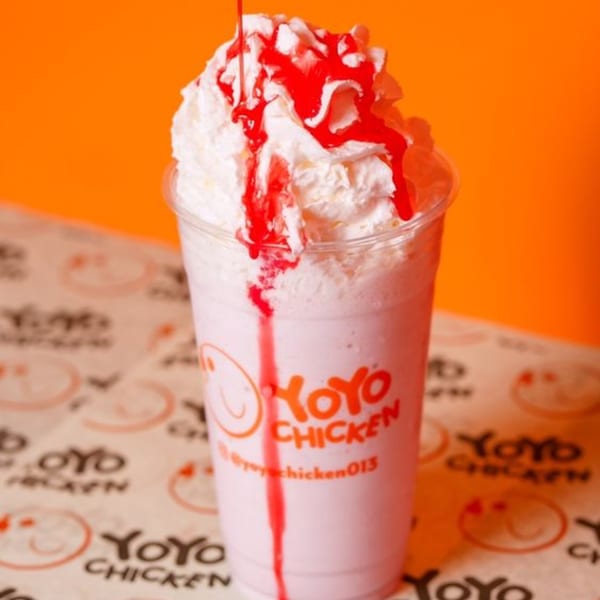 Yoyo Chicken strawberry milkshake with whipped cream and red syrup on branded paper.