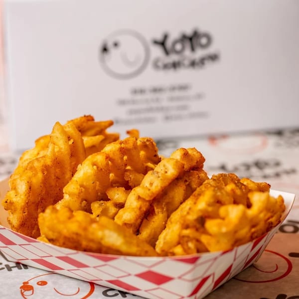 Crispy, seasoned waffle fries in a red and white checkered paper tray from Yoyo Chicken.