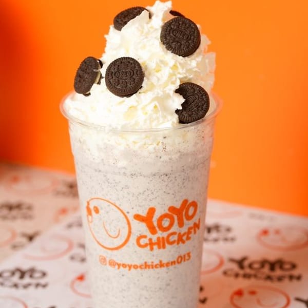 Yoyo Chicken's cookies and cream milkshake with whipped cream and Oreo cookies on an orange background.