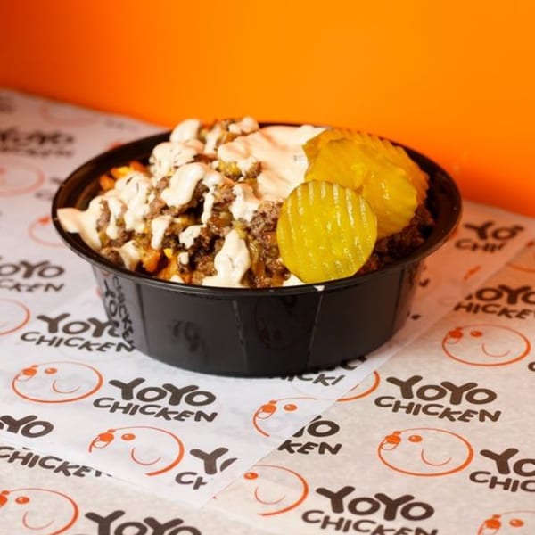 Yoyo Chicken's loaded fries with ground meat, white sauce, and pickles in a black bowl.
