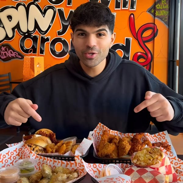A man in a black hoodie points to multiple baskets of Yoyo Chicken fried chicken, fries, and sandwiches.