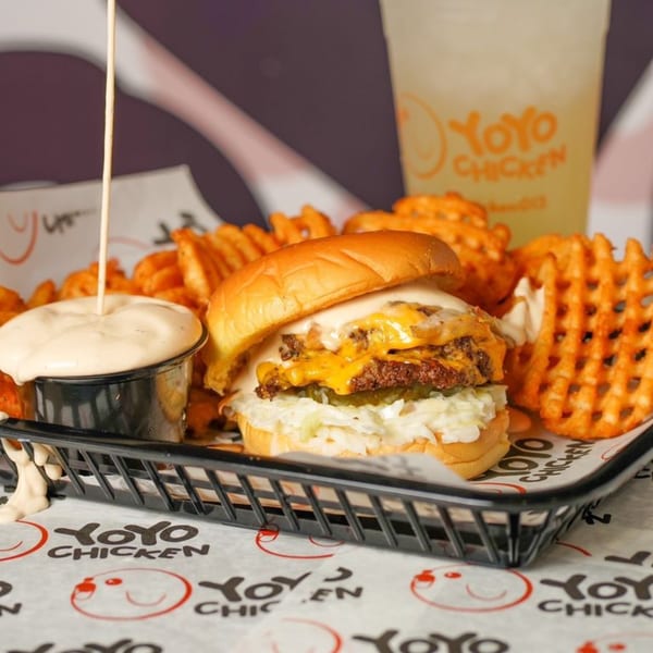 Yoyo Chicken burger with melted cheese, waffle fries, and dipping sauce in a black basket.