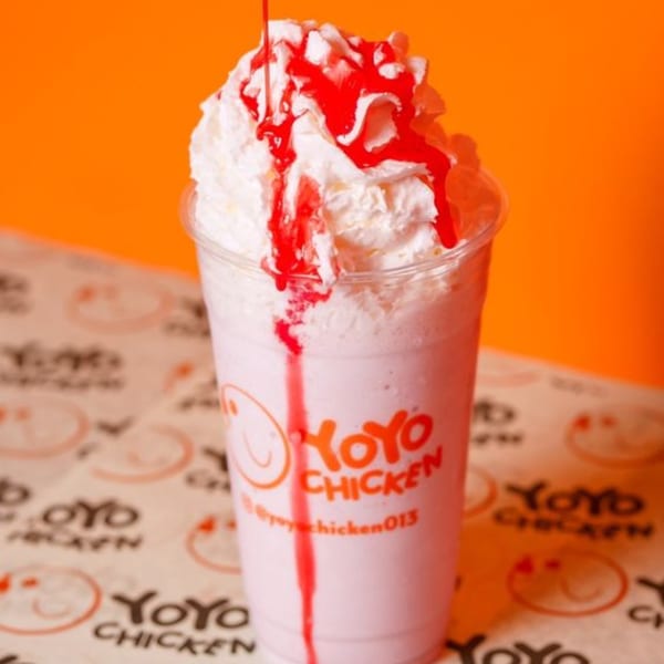 A Yoyo Chicken strawberry milkshake with whipped cream and red syrup drizzle on a branded paper.