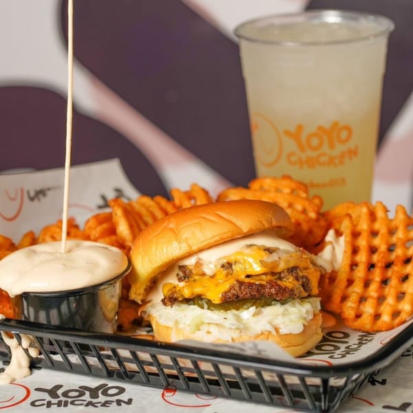 Yoyo Chicken cheeseburger with waffle fries, dipping sauce, and a drink in a black basket.