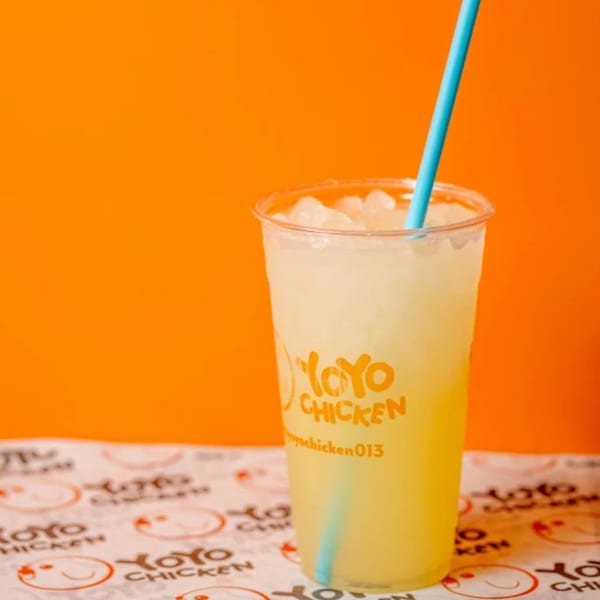 A Yoyo Chicken branded cup filled with a light yellow drink and ice, with a blue straw.