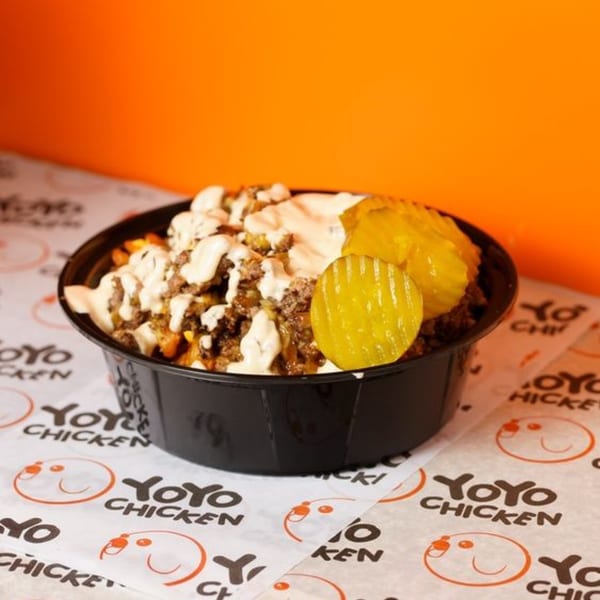 Yoyo Chicken's loaded fries with ground meat, white sauce, and pickles in a black bowl.