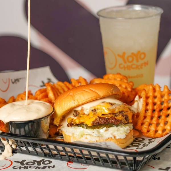 Yoyo Chicken burger with waffle fries, dipping sauce, and a drink in a black basket.
