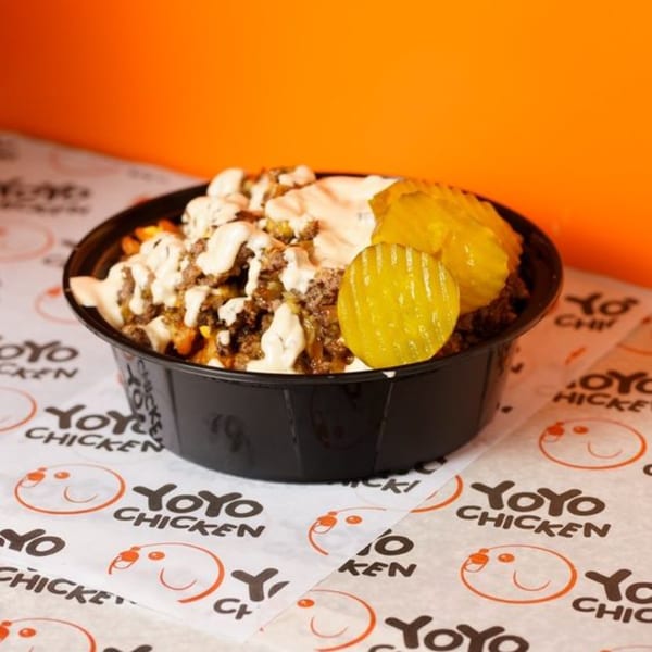 A black bowl of Yoyo Chicken's loaded fries with sauce, ground meat, and pickles.