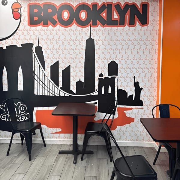 Yoyo Chicken's dining area with black tables and chairs against a Brooklyn skyline mural.