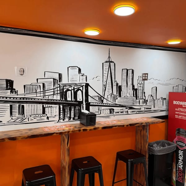A Yoyo Chicken counter with a New York City skyline mural, stools, and orange walls.