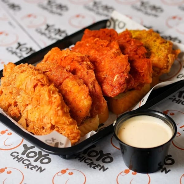 A black tray of Yoyo Chicken's fried chicken tenders in various flavors, with a side of dipping sauce.