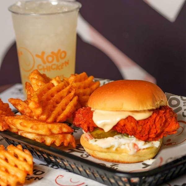 A Yoyo Chicken fried chicken sandwich with waffle fries and a drink in a black basket.