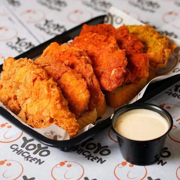 A black tray of Yoyo Chicken's fried chicken tenders in various flavors, with a side of dipping sauce.