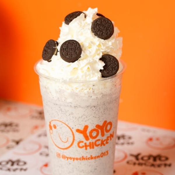 Yoyo Chicken's Oreo milkshake, topped with whipped cream and whole Oreo cookies, against an orange background.