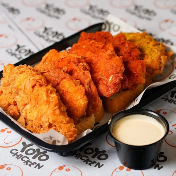 A black tray of Yoyo Chicken fried chicken tenders in various flavors with a side of dipping sauce.