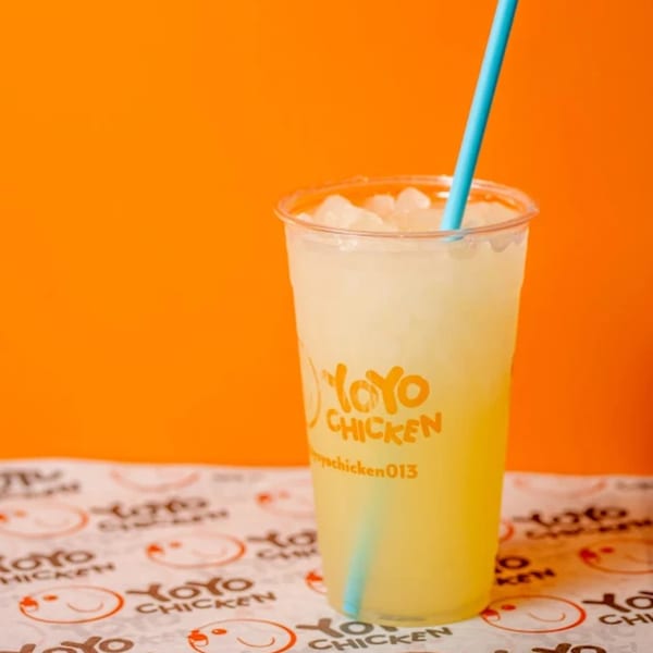 A Yoyo Chicken branded lemonade with ice and a blue straw, on branded paper with an orange background.
