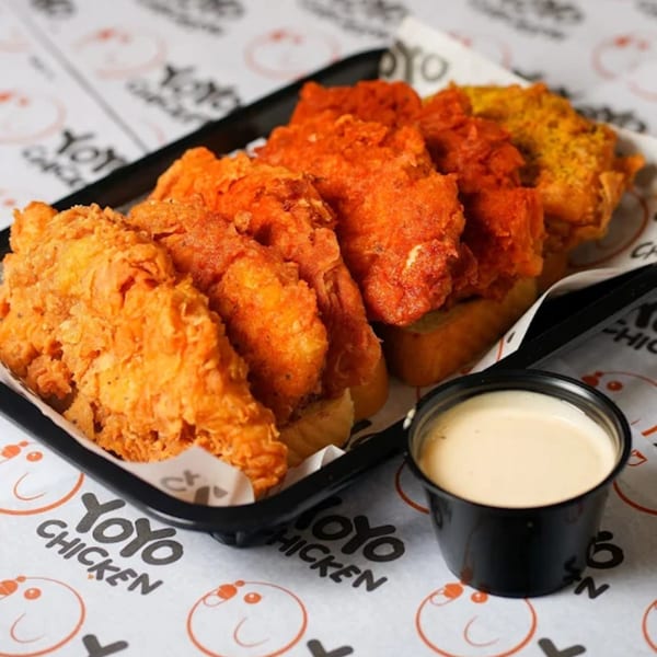 A black tray of Yoyo Chicken's fried chicken tenders in various flavors, with a side of sauce.