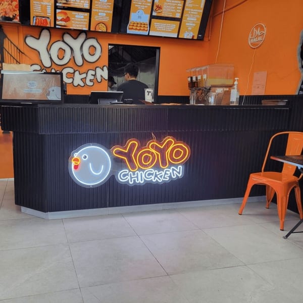 Yoyo Chicken counter with a neon chicken logo, orange walls, and menu boards.