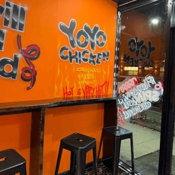 Yoyo Chicken restaurant interior with orange walls, black bar stools, and a window reflecting street lights.