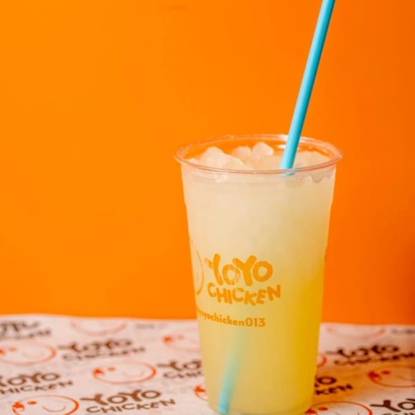 A Yoyo Chicken branded cup of lemonade with ice and a blue straw, on a patterned paper.