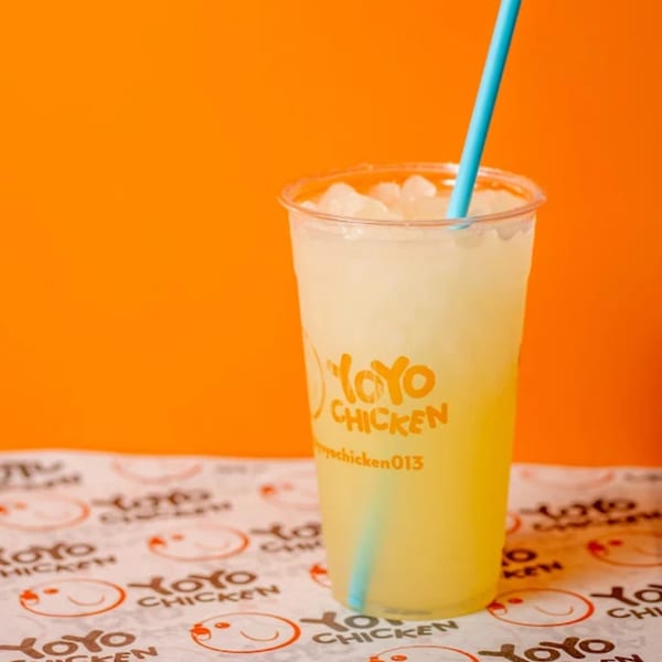 A Yoyo Chicken branded cup of iced lemonade with a blue straw on a branded paper liner.
