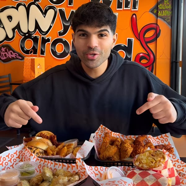 Man pointing at a table full of Yoyo Chicken fried chicken, burgers, fries, and sauces.