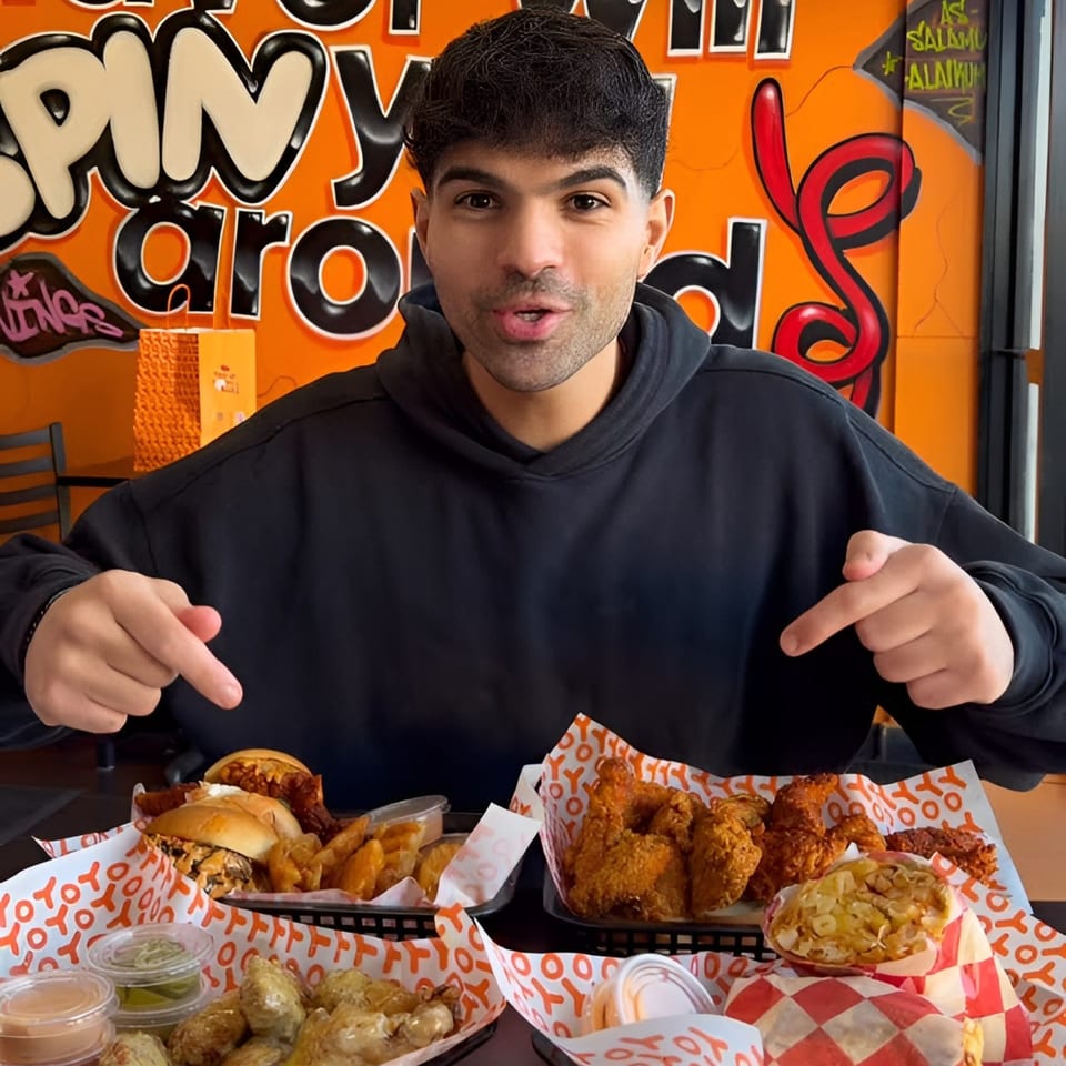 Man pointing at a table full of Yoyo Chicken fried chicken, burgers, fries, and sauces.