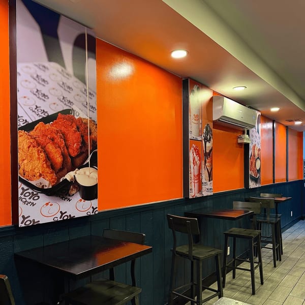 Interior of Yoyo Chicken with orange walls, dark tables, and large fried chicken menu posters.