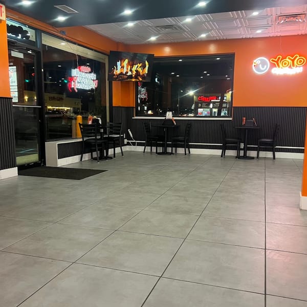 Empty Yoyo Chicken restaurant interior with black tables, chairs, and an orange neon logo.