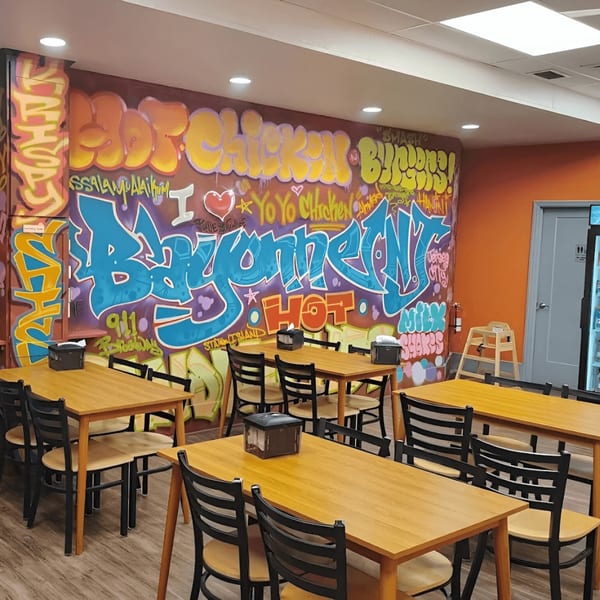 Yoyo Chicken's dining area with wooden tables, black chairs, and a colorful graffiti wall.