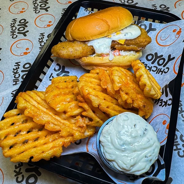 Yoyo Chicken's fried chicken sandwich with waffle fries and a side of dipping sauce in a black basket.
