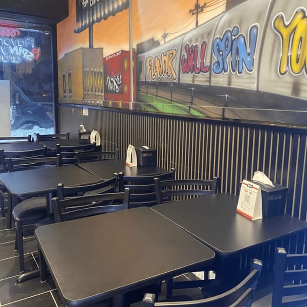 Interior of Yoyo Chicken with black tables and chairs, and a colorful mural of a train on the wall.